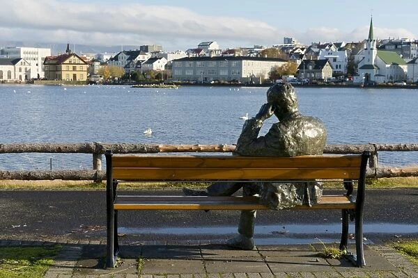Sculpture of a man sitting on a park bench in front of Tjornin Lake and the Historic