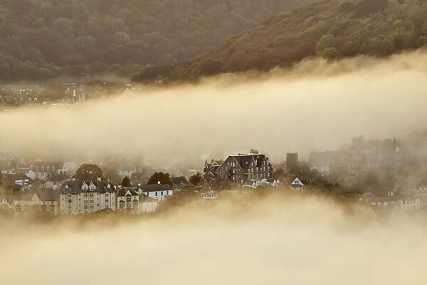 Sea fog envelops the coastal town of Lynton, lit by the light of sunset, seen from Countisbury Hill, Exmoor National Park, Devon, England, United Kingdom, Europe