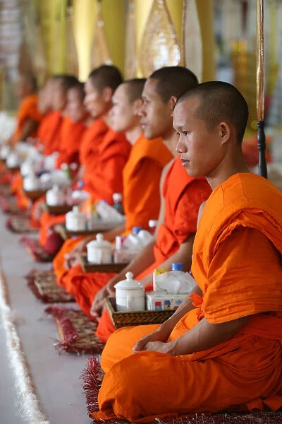 Seated Buddhist monks chanting and reading prayers at a ceremony