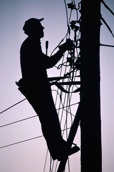 Silhouette of engineer working up a telegraph pole, East Sussex, England