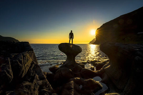 Silhouette of man admiring sunset standing on top of Kannesteinen rock, Oppedal, Vagsoy