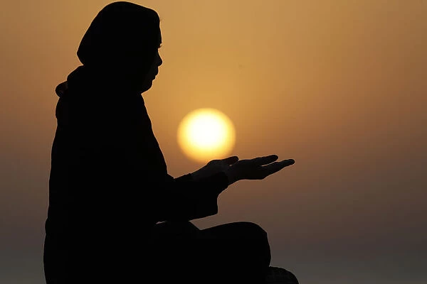 Silhouette of a Muslim woman in abaya praying with her hands at sunset