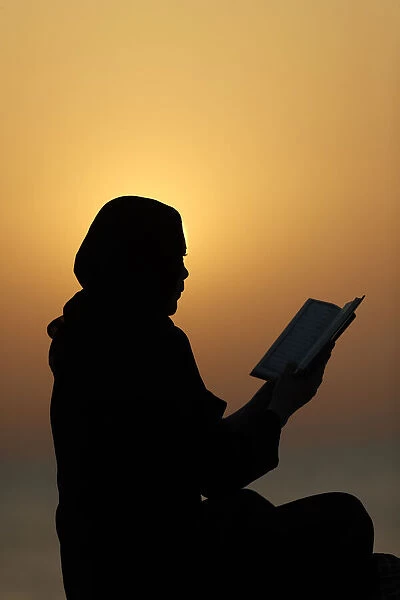 Silhouette of a Muslim woman reading the Noble Quran at sunset, United Arab Emirates