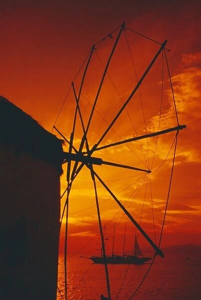 Silhouette of a windmill at sunset and boat in the background