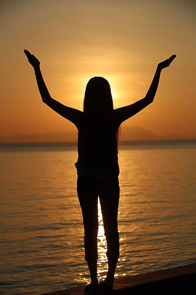 Silhouette of a woman standing by the sea at sunset doing yoga pose and meditation, Kep