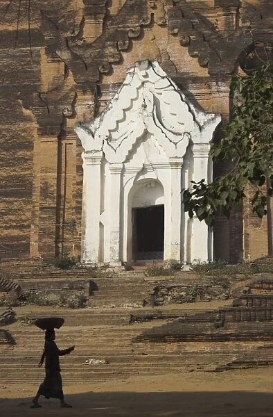 Silhouette of a woman with tray on her head walking past stupa entrance