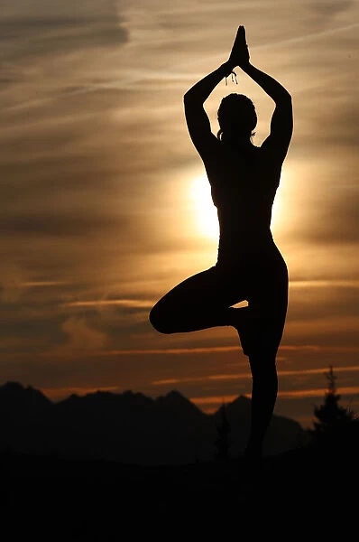 Silhouette of a woman in Vrkasana (tree pose) practising yoga against the light of the