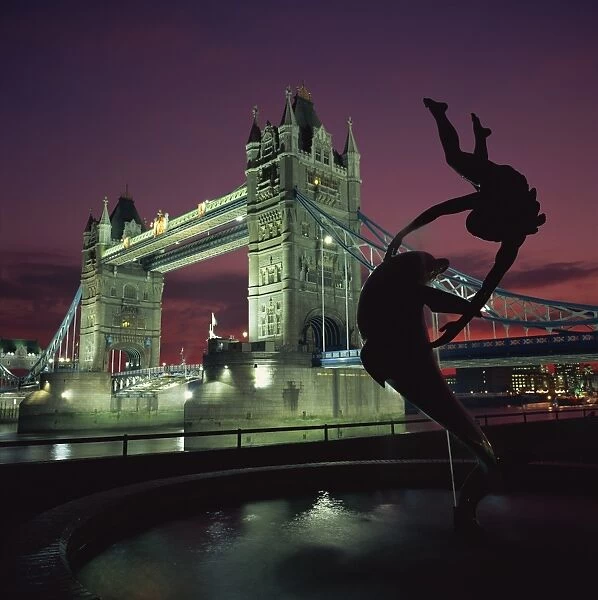 Silhouetted fountain statue and Tower Bridge illuminated at night, London
