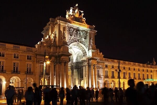 Silhouetted people on Praca do Comercio under the illuminated Rua Augusta Arch at night in central Lisbon