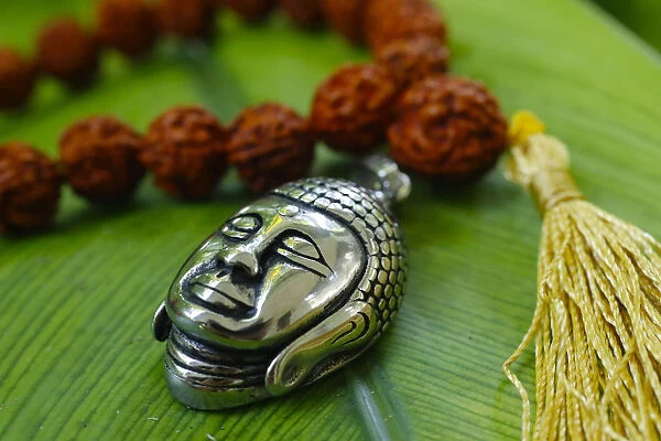 Silver Buddha medallion and prayer beads (mala) on a green leaf, Kep, Cambodia, Indochina