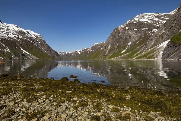 Snow capped mountains reflected in the still waters of the fjord where kayakers are