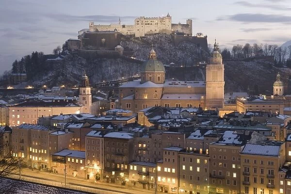 Snow covered Old Town with towers of Glockenspiel, Dom and Franziskanerkirche churches dominated by the fortress of Festung Hohensalzburg at twilight, Salzburg