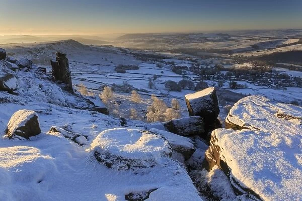 Snow on millstone lit by sunrise, Curbar and Baslow Edge with misty hills and wintry trees, Peak District, Derbyshire, England, United Kingdom, Europe