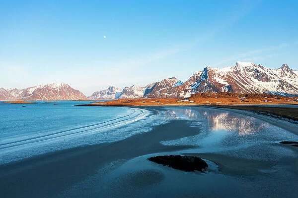 Snowcapped mountains reflected on Fredvang beach washed by waves at sunset, Nordland county, Lofoten Islands, Norway, Europe