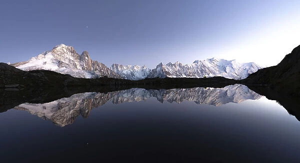 Snowy peaks of Mont Blanc massif mirrored in the clear water of Lacs de Cheserys at dusk