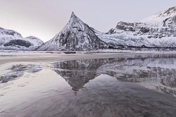 Snowy peaks reflected in the frozen sea surrounded by sandy beach at dawn, Ersfjord