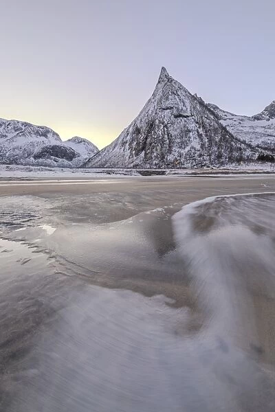 Snowy peaks and sandy beach framed by the icy waves of frozen sea at dawn, Ersfjord