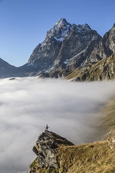 A solitary hiker admiring the profile of the Monviso (Monte Viso) emerging from the fog, Piedmont, Italy, Europe