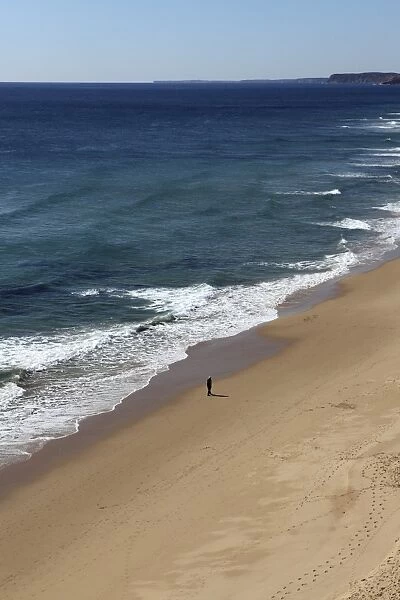 A solitary man walks an otherwise empty golden beach, on the Atlantic coastline, near Lagos, Algarve, Portugal, Europe