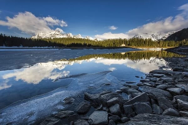 The spring thaw melts ice while snowy peaks are reflected in Lake Palu, Malenco Valley
