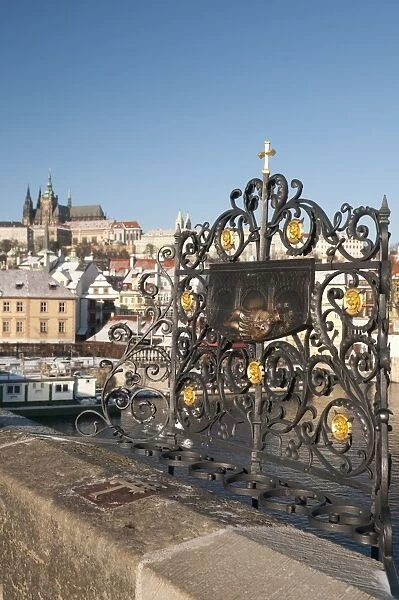 St. John of Nepomuk (Jan Nepomucky) shrine with cross at Charles Bridge with snow-covered Prague Castle and Mala Strana in background, UNESCO World Heritage Site, Prague, Czech