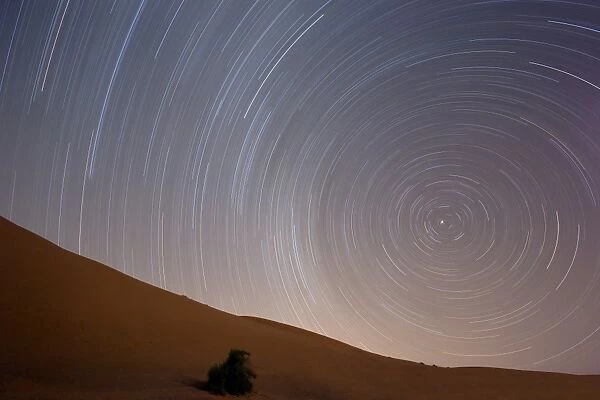 Star trails in night sky around Polaris (the pole star) over dunes of the Erg Chebbi