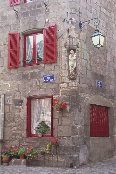 Statue of the Madonna and Child on a house with red shutters on a street corner in Besse en Chandesse, in the Auvergne