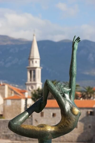 Statue of naked dancing girl on a rock with Budva old town in the background