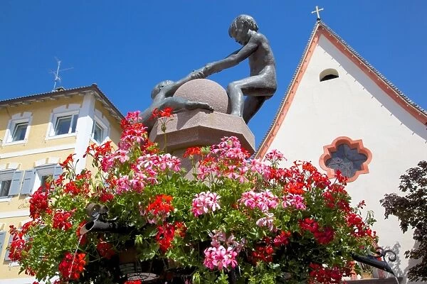 Statues and geraniums in Town Square, Ortisei, Gardena Valley, Bolzano Province, Trentino-Alto Adige  /  South Tyrol, Italian Dolomites, Italy, Europe