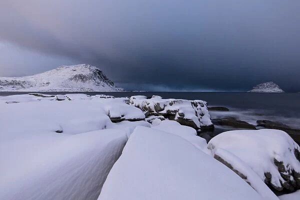 Storm clouds on the snowy peaks reflected in the cold sea at night, Haukland, Lofoten Islands