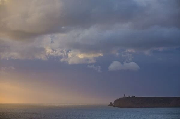 Stormy sunset over Atlantic ocean and cliffs at Cape St. Vincent with lighthouse in the distance
