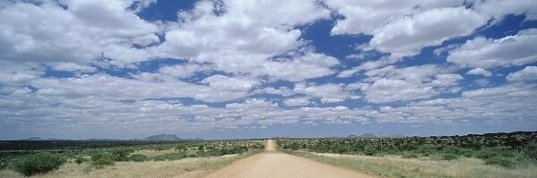 Straight gravel road cutting across grassy plain near Windhoek