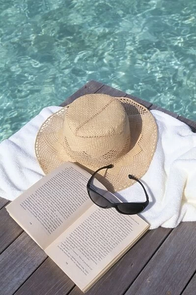 Straw hat, book and sunglasses on towel