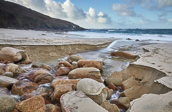 A stream cuts through sand and rocks as it makes its final dash to the sea, Portheras Cove, a remote cove on the Atlantic Coast, near Pendeen, in the far west of Cornwall, England, United Kingdom, Europe