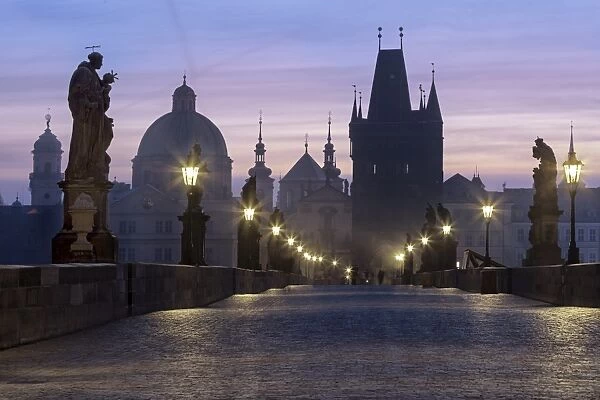 Street lanterns and old statues frame the historical buildings on Charles Bridge at dawn
