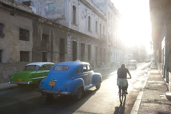 Street scene bathed in early morning sunlight showing old American cars and cyclists