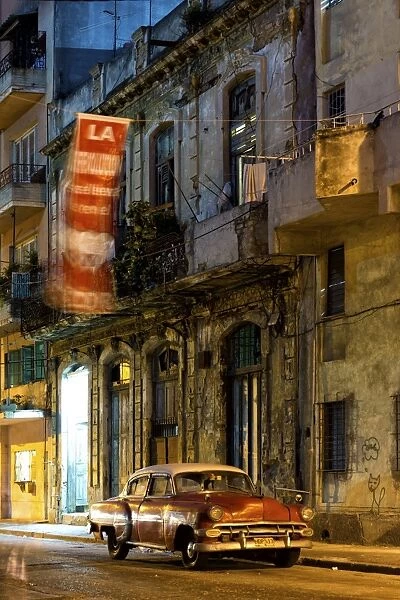 Street scene at night lit by artificial lighting with vintage American car and fluttering revolutionary banner, Havana Centro, Havana, Cuba, West Indies, Central America