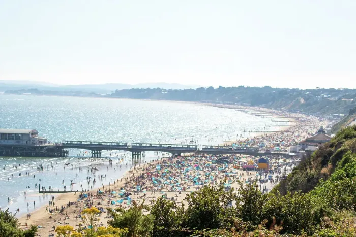 Framed Print : Sunny beach day with crowded sandy shore and pier, clear blue water, and lush greenery in the foreground in Bournemouth, Dorset, England, United Kingdom, Europe Framed Print : Sunny beach day with crowded sandy shore and pier, clear blue water, and lush greenery in the foreground in Bournemouth, Dorset, England, United Kingdom, Europe