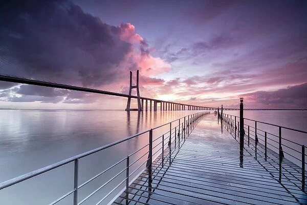 Sunrise colors the clouds reflected in Tagus River and frame the Vasco da Gama bridge in Lisbon