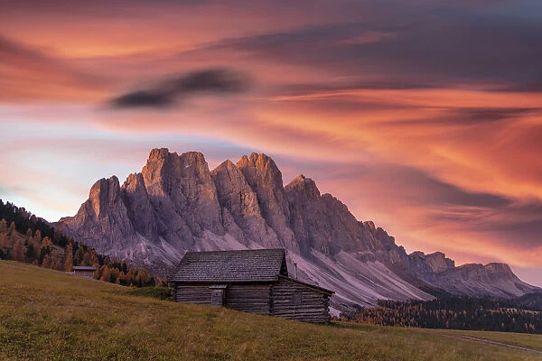 Sunrise over the Odle peaks and traditional hut in Gampen Alm in autumn, Funes Valley