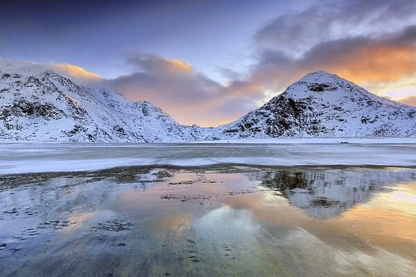 Sunrise on Uttakleiv beach surrounded by snow covered mountains reflected in the cold sea