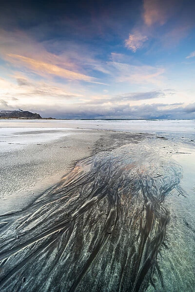 Sunset over the black sand of Skagsanden beach covered with ice in winter, Flakstad