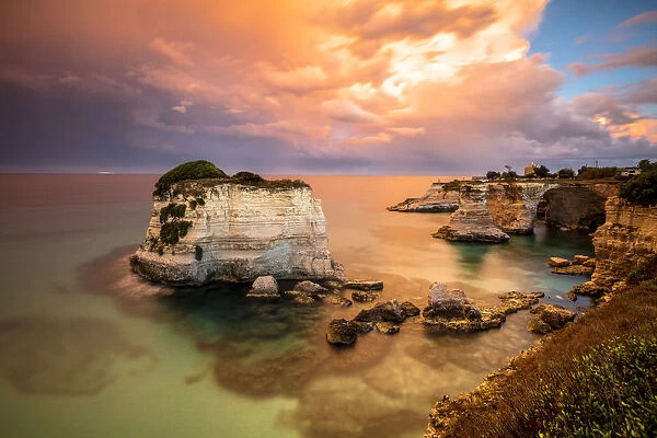 Sunset frames the high cliffs known as Faraglioni di Sant Andrea and the turquoise sea