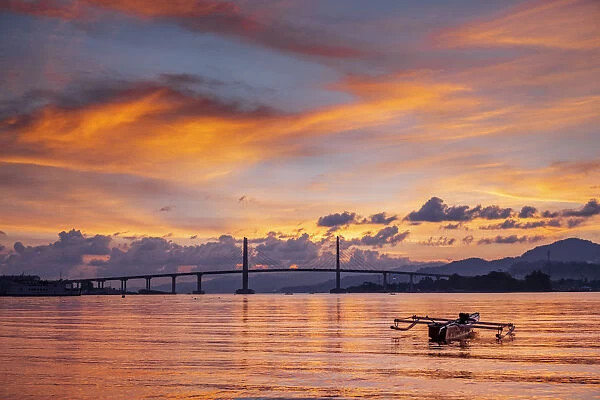 Sunset over the harbour in Ambon city showing the suspension bridge and an outrigger boat
