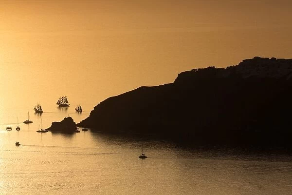 Sunset over the sea with boats and cliffs in silhouette near Oia, from Imerovigli