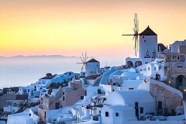 Sunset over the white stone buildings and windmills of Oia on the tip of Santorinis caldera