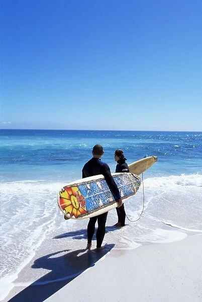 Two surfers walking with their boards on Kommetjie beach