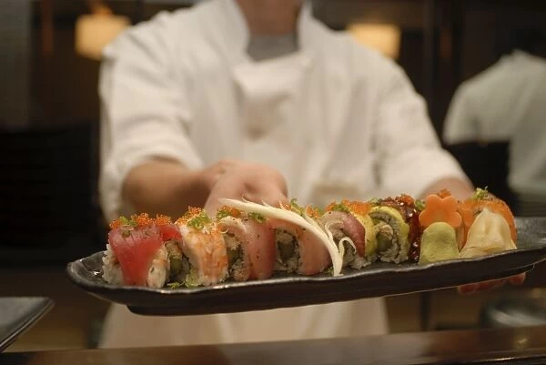 Sushi chef presents a plate of various seafood sushi