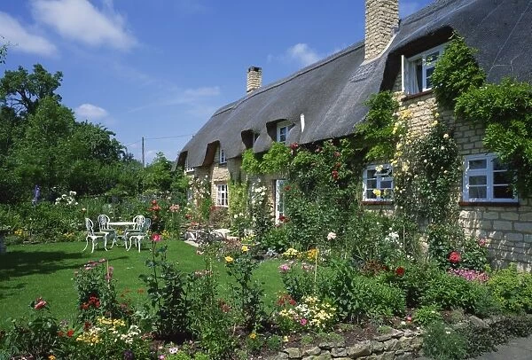 Thatched cottages with roses on the walls and gardens with summer flowers in the Cotswolds