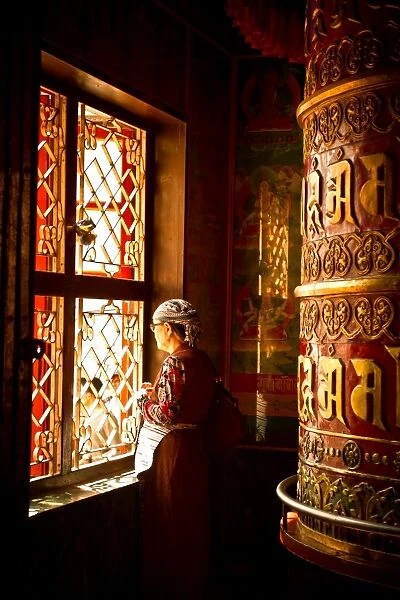 A Tibetan woman stands next to a large prayer wheel of the temple of Boudhanath Stupa